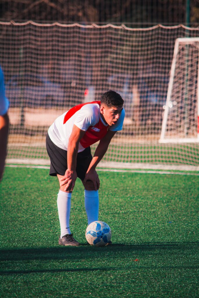 A tired soccer player resting on the field, showing fatigue and determination in a sports match.