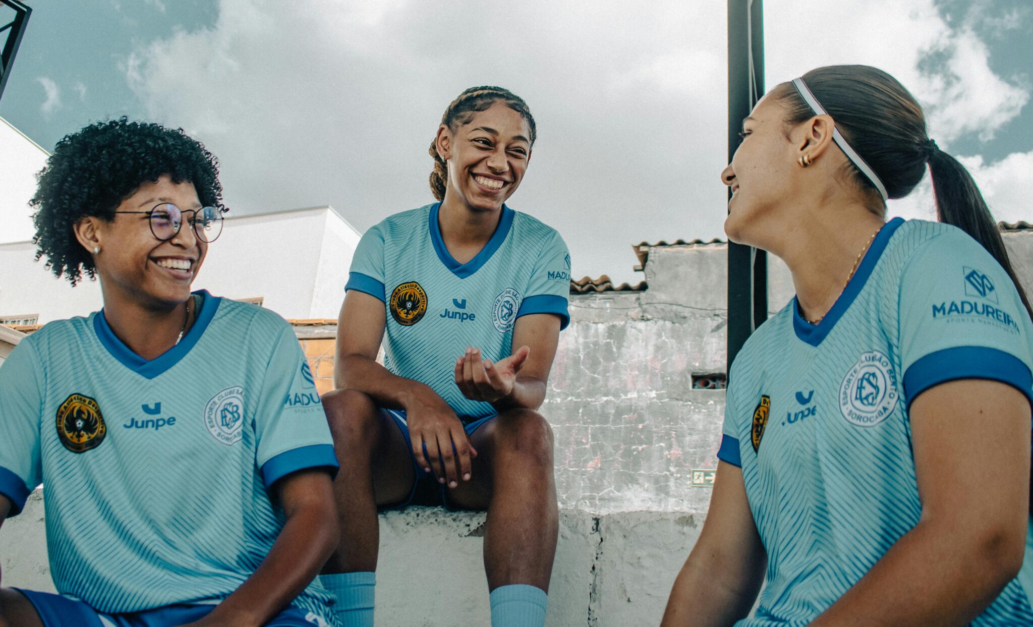 Three female soccer players share a lighthearted moment outdoors, embodying teamwork and joy.
