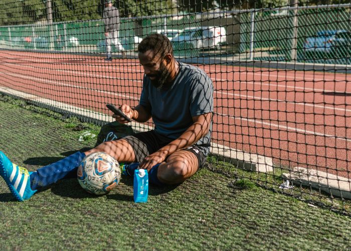 pexels-photo-7187884-7187884 Athlete taking a break on a soccer field with ball and smartphone, enjoying leisure time.